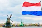 为什么荷兰国旗不是橙色的?红、白、蓝三色旗帜的图片，背景是风车